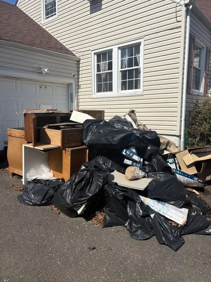 Furniture, bagged waste and boxes stacked beside a garage